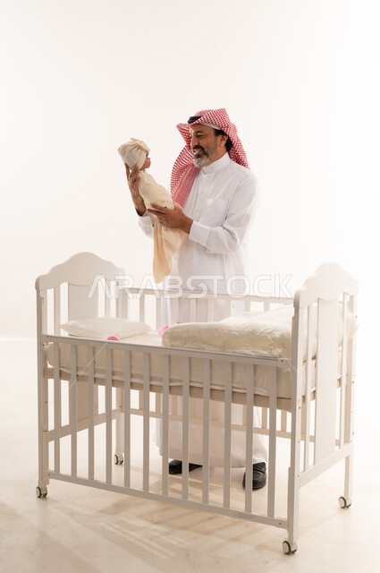 رجل سعودي يحمل طفلاً حديث الولادة بجانب السرير