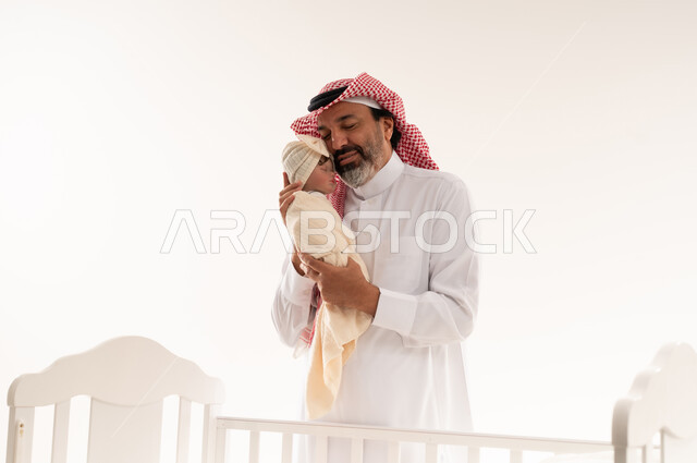 أب سعودي يحمل طفله المولود بجانب سرير أبيض