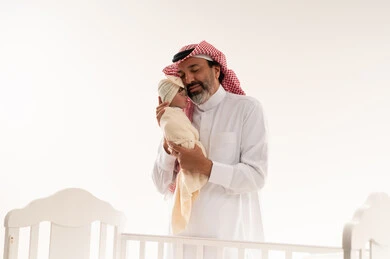 Saudi Father Holding Newborn Baby in White Nursery