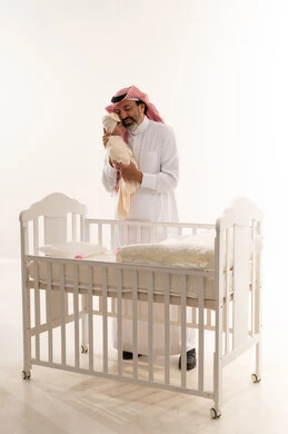 أب سعودي يحمل طفلاً حديث الولادة بجانب سرير
