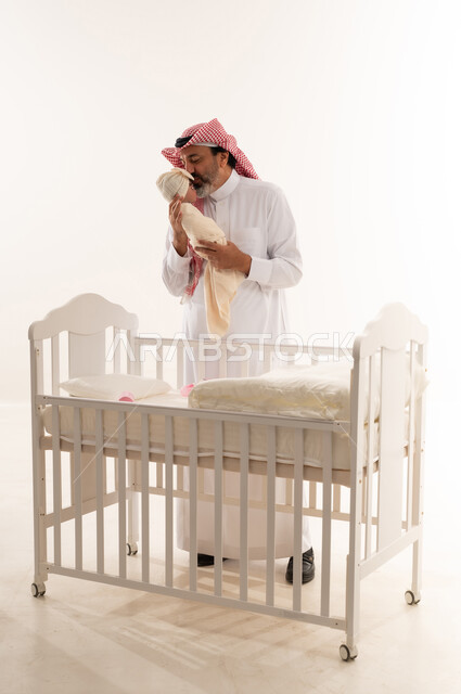 أب سعودي يقبل طفله الرضيع بجانب سرير أبيض