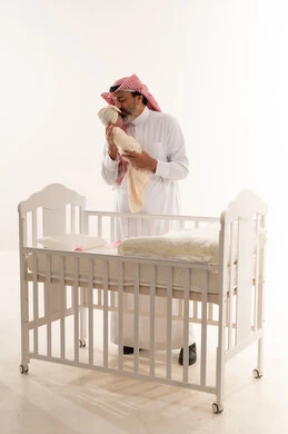أب سعودي يقبل طفله الرضيع بجانب سرير أبيض