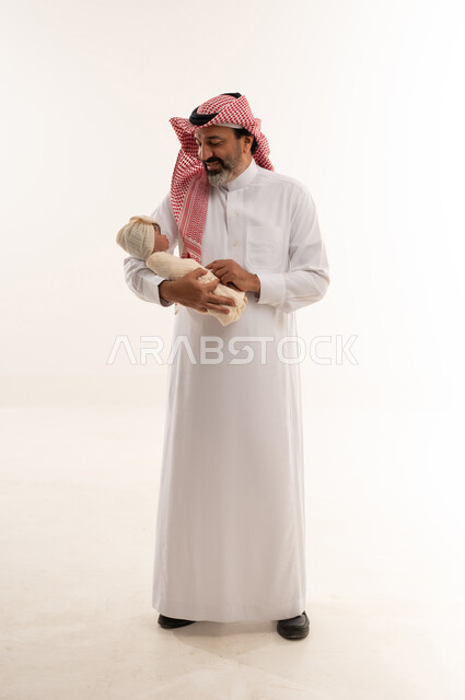 رجل سعودي يحمل طفلاً حديث الولادة في استوديو