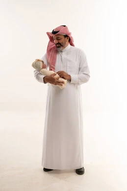 رجل سعودي يحمل طفلاً حديث الولادة في استوديو