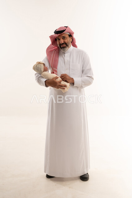 رجل سعودي يحمل طفلاً حديث الولادة في الاستوديو