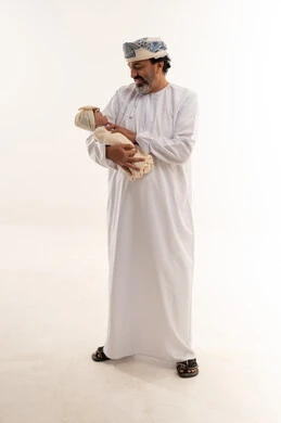 أب عُماني بالزي التقليدي يحمل طفله حديث الولادة