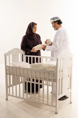 والدان عمانيان يحملان مولوداً جديداً بجانب سرير أبيض