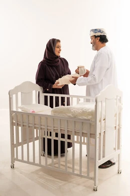 والدين عمانيين مع مولود جديد وسرير طفل أبيض