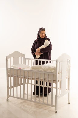 Saudi Grandmother Holding Newborn Baby by Crib