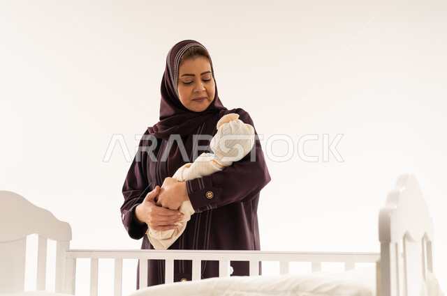 جدة عربية تحمل طفلاً حديث الولادة بجانب مهد أبيض
