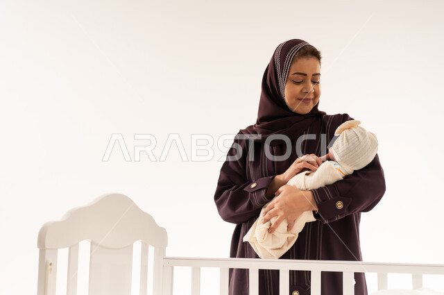 أم سعودية تحمل مولودها الجديد بجانب سرير أبيض