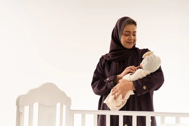Saudi Mother Holding Newborn Baby Next to White Crib