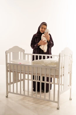 أم عربية تحمل طفل رضيع بجانب سرير أبيض