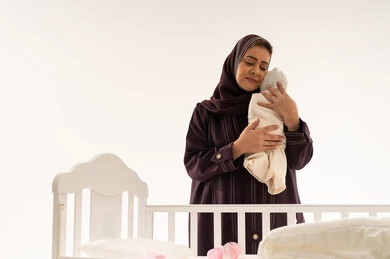 Saudi Woman Holding Swaddled Newborn Baby by White Crib