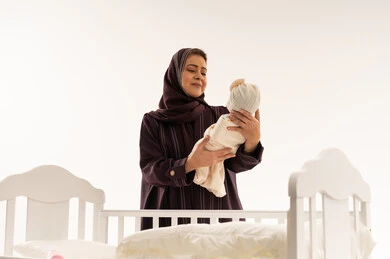 أم سعودية تحمل مولوداً جديداً بجانب مهد أبيض