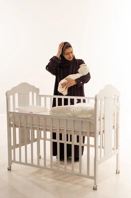Exhausted Emirati Mother Holding Newborn Baby Near Crib
