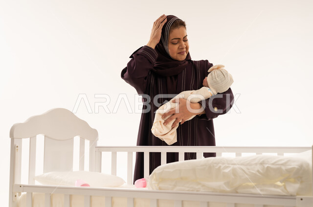 أم سعودية متعبة تحمل طفلها بجانب سرير أبيض