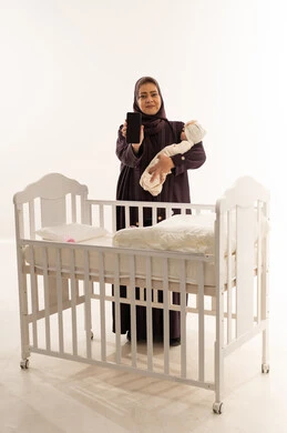 Saudi Woman with Baby Holding Smartphone by Crib