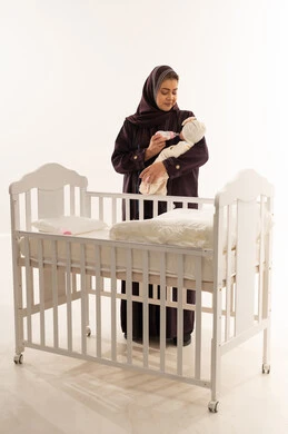 Arab Mother Bottle Feeding Infant Behind White Crib