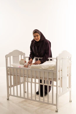 Saudi Grandmother Tending to Newborn in White Crib