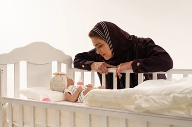 Arab Mother Looking at Newborn Baby in White Crib
