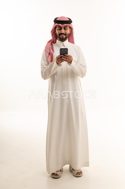 رجل سعودي بالثوب التقليدي يستخدم الهاتف الذكي بخلفية بيضاء