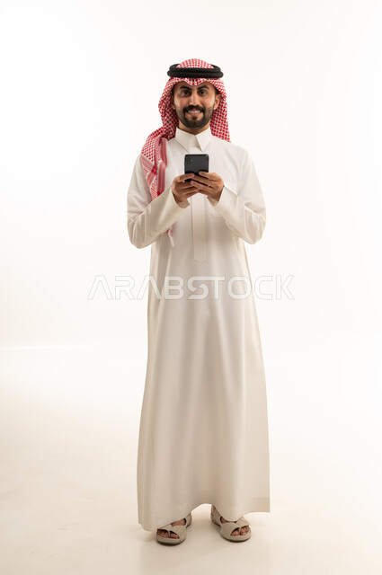 رجل سعودي بالثوب التقليدي يستخدم الهاتف الذكي