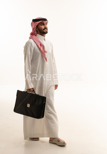 رجل أعمال سعودي يمشي بحقيبة عمل على خلفية بيضاء