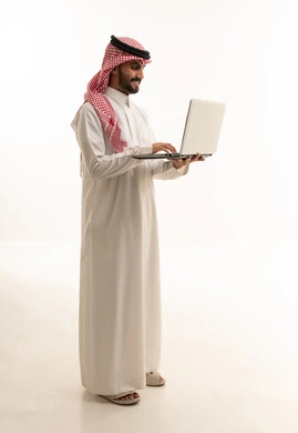 رجل سعودي مبتسم يستخدم الحاسوب المحمول بخلفية بيضاء