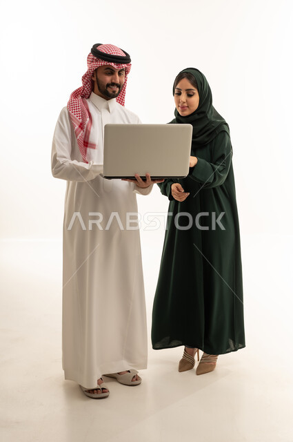رجل وامرأة سعوديان يستخدمان الكمبيوتر في استوديو أبيض