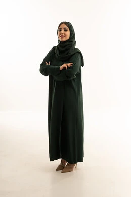 امرأة سعودية بعباءة خضراء تقف في الاستوديو