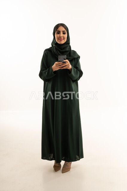 امرأة سعودية بعباءة خضراء تمسك بهاتف ذكي