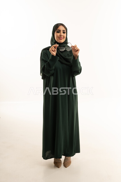 امرأة سعودية بعباءة خضراء تمسك بنظارة طبية في استوديو