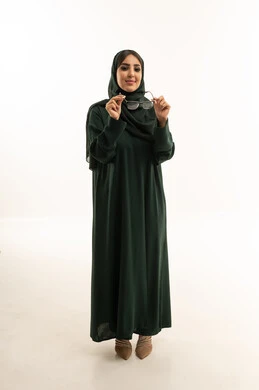 امرأة سعودية بعباءة خضراء تمسك بنظارة طبية في استوديو