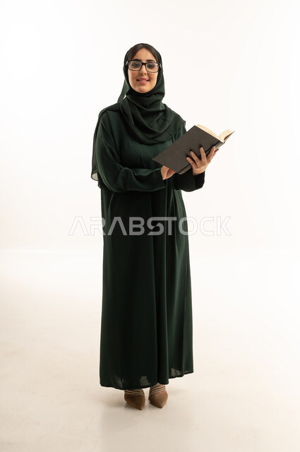 امرأة سعودية بعباءة خضراء تحمل كتاباً في استوديو