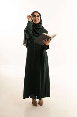 امرأة عربية بعباءة خضراء تمسك كتابا في الاستوديو