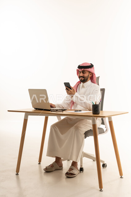 رجل أعمال سعودي يستخدم الكمبيوتر والجوال في المكتب