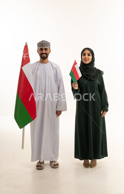 رجل وامرأة بزي عماني تقليدي يحملان علم عمان