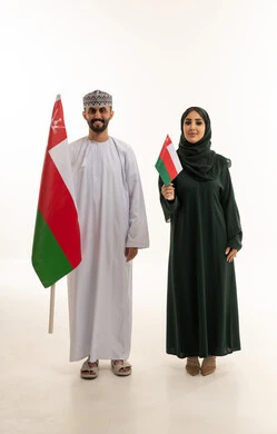 رجل وامرأة بزي عماني تقليدي يحملان علم عمان