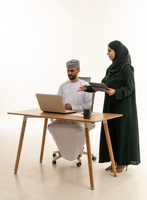 زملاء عمل عمانيون يعملون على المكتب مع كمبيوتر محمول