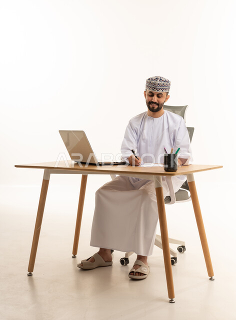 رجل عماني يكتب على مكتب عمل مع لابتوب