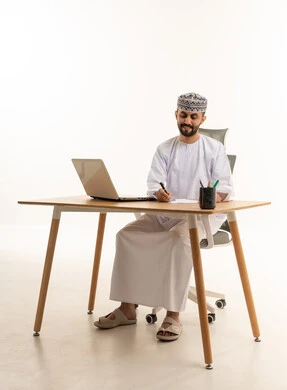 رجل عماني يكتب على مكتب عمل مع لابتوب