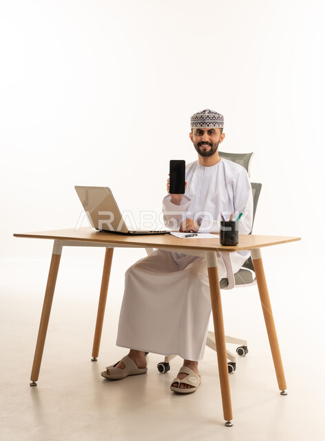 Omani Man at Desk Holding Smartphone Blank Screen