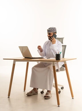 رجل أعمال عُماني على مكتب مع كمبيوتر وهاتف