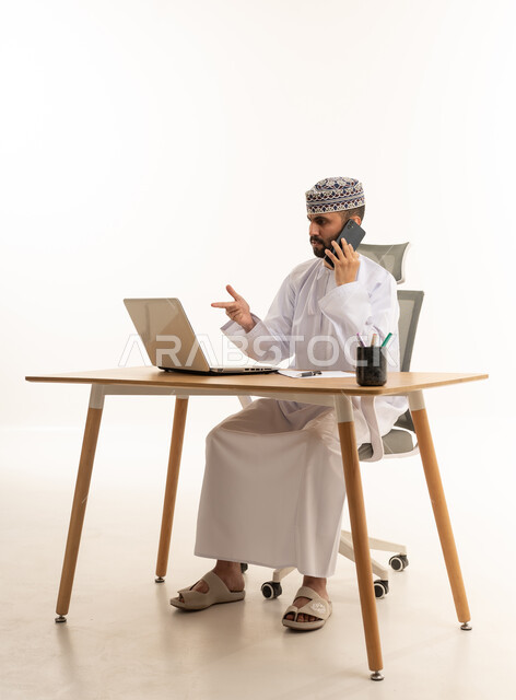 Omani Businessman Using Laptop and Phone on White Background