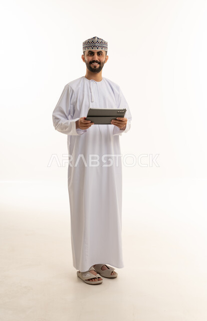 رجل عُماني بالزي التقليدي يحمل جهازاً لوحياً
