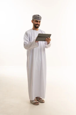 رجل عماني بالزي التقليدي يستخدم جهاز لوحي بخلفية بيضاء
