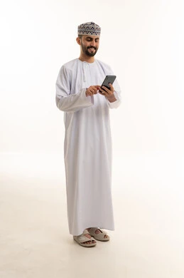 رجل عماني بالدشداشة التقليدية يستخدم الهاتف الذكي