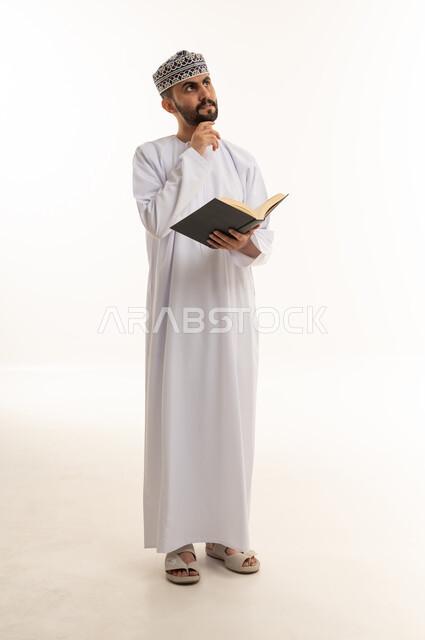 رجل عماني بالزي التقليدي يقرأ كتاب ويفكر