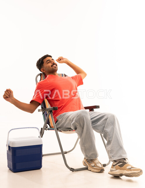 شاب سعودي يسترخي على كرسي تخييم مع صندوق تبريد
